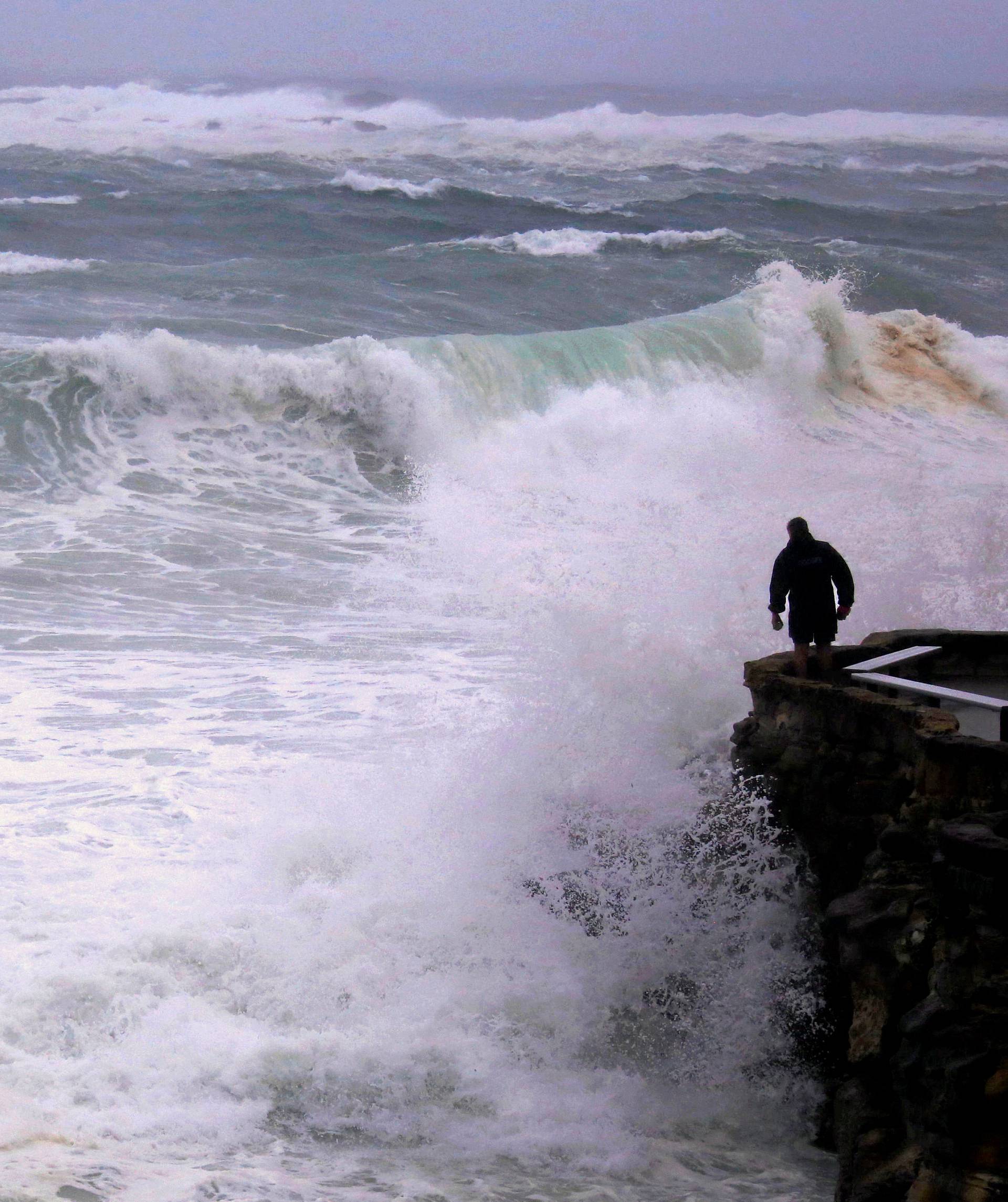 A man looks over cliff as large waves batter coastline near Coogee Beach in Sydney