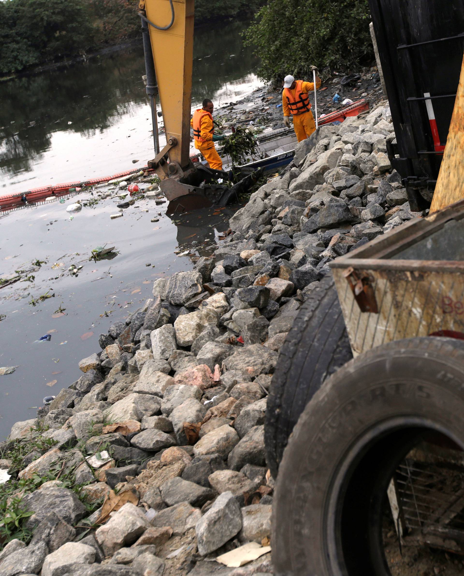 Men work cleaning up the garbage next to an ecobarrier at Meriti River which flows into Guanabara Bay, in Duque de Caxias, near Rio de Janeiro