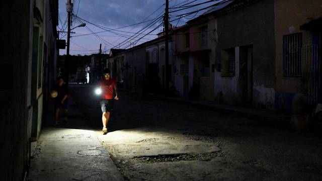 A young man illuminates his way with the lamp of his mobile phone during a power outage in Bejucal