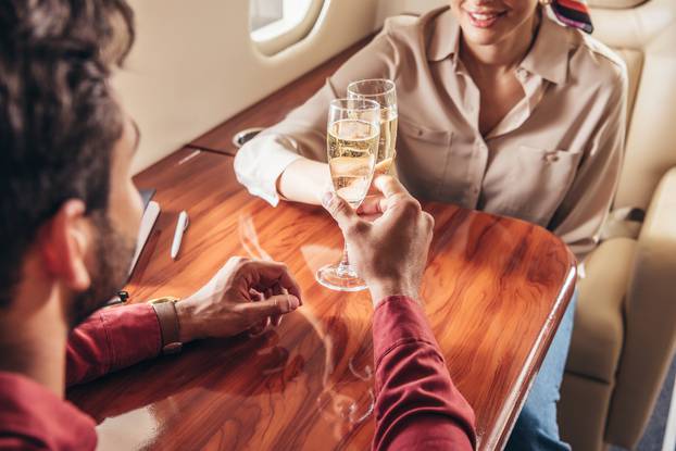 boyfriend and girlfriend clinking with champagne glasses in private plane 