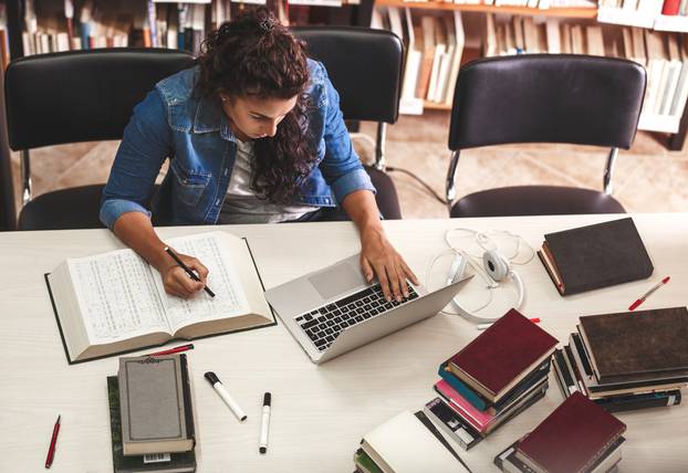 Young,Female,Student,Study,In,The,School,Library.she,Using,Laptop