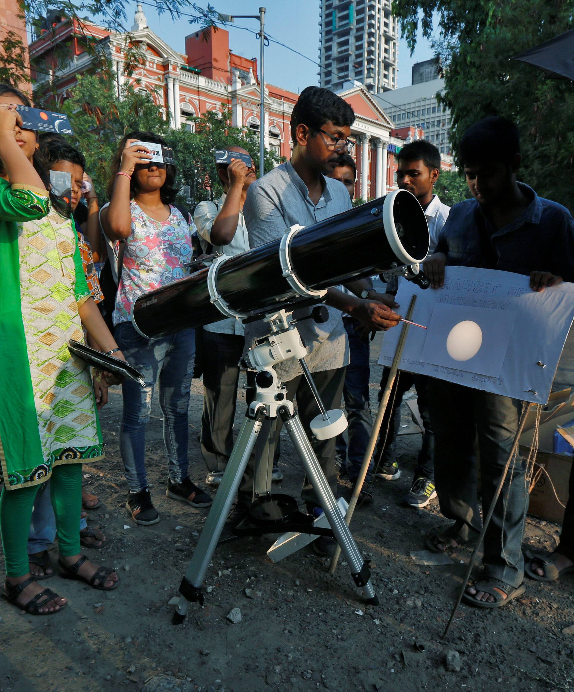 People look at planet Mercury transiting across the sun with solar filters at a public viewing in Kolkata