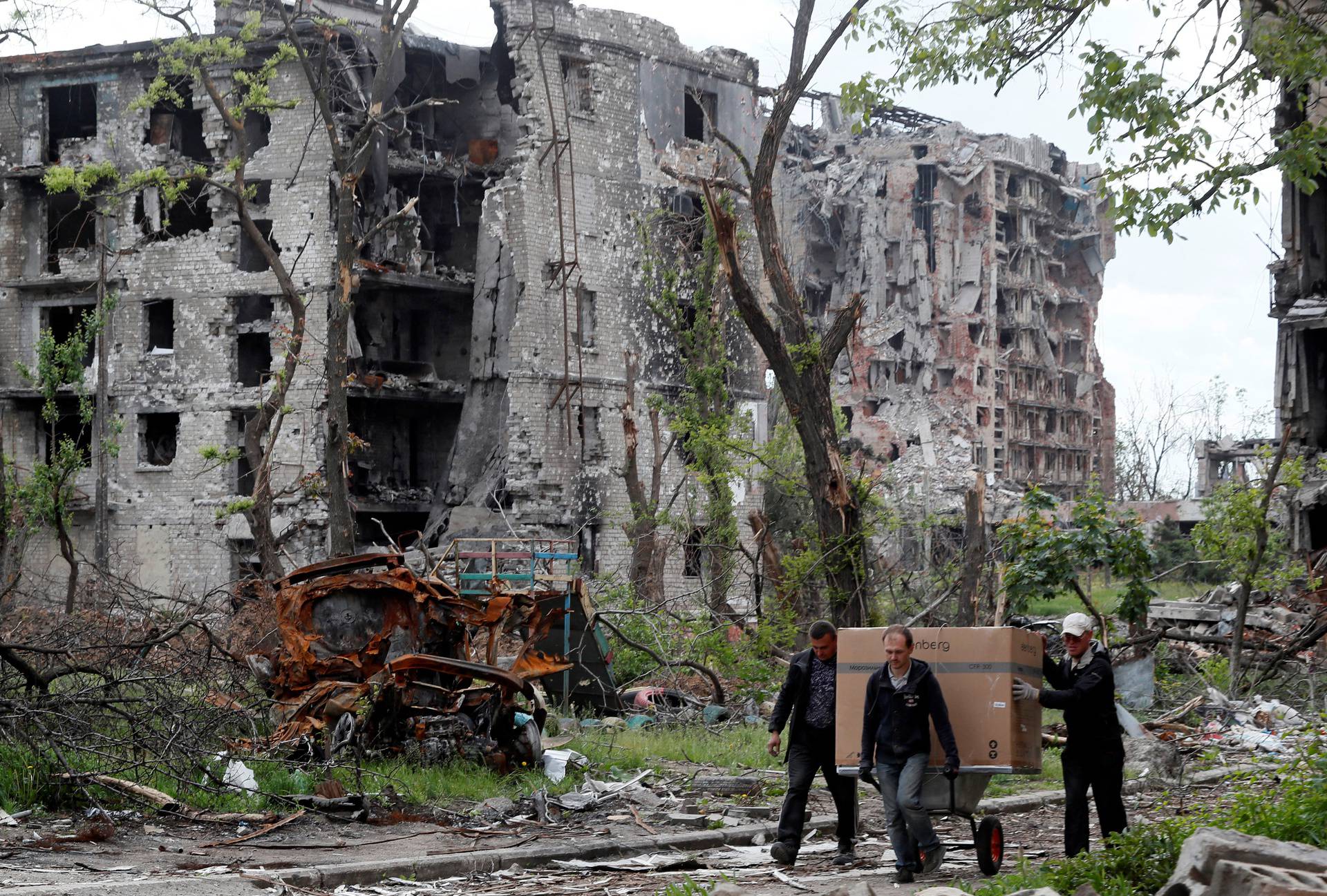 Local residents transport a box on a wheelbarrow past a heavily damaged apartment building in Mariupol