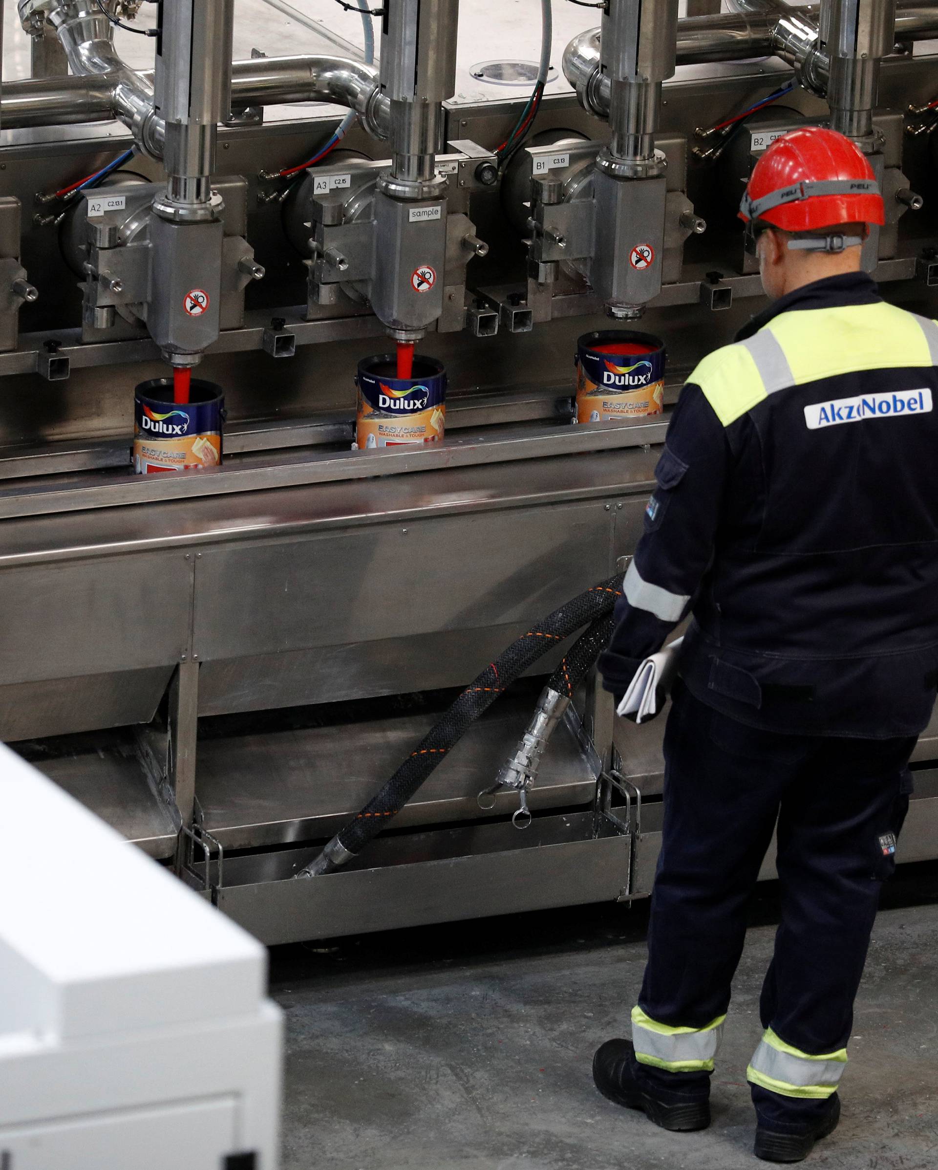 Workers look on as Dulux paint cans are filled on the production line inside AkzoNobel's new paint factory in Ashington, Britain