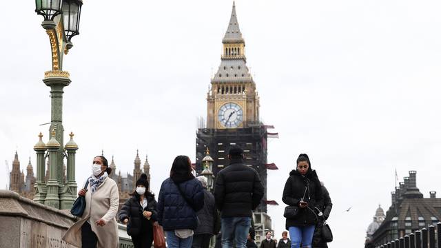 People wearing protective face masks walk over Westminster Bridge in front of the Elizabeth Tower, more commonly known as Big Ben, in London