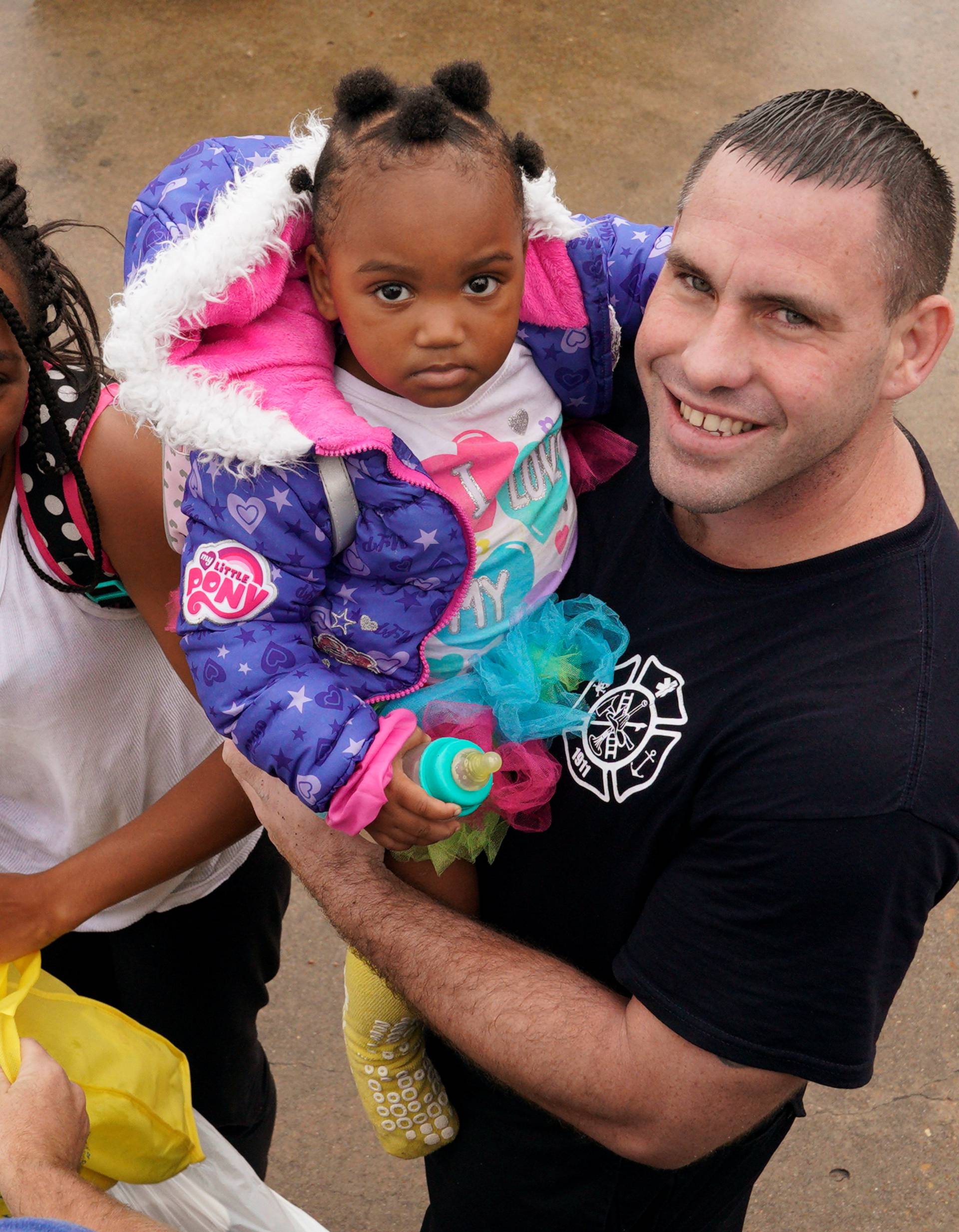 Texas City fire fighter/paramedic Allen Jacobs holds a little girl with her mother after he evacuated them from Hurricane Harvey floodwaters in Dickinson