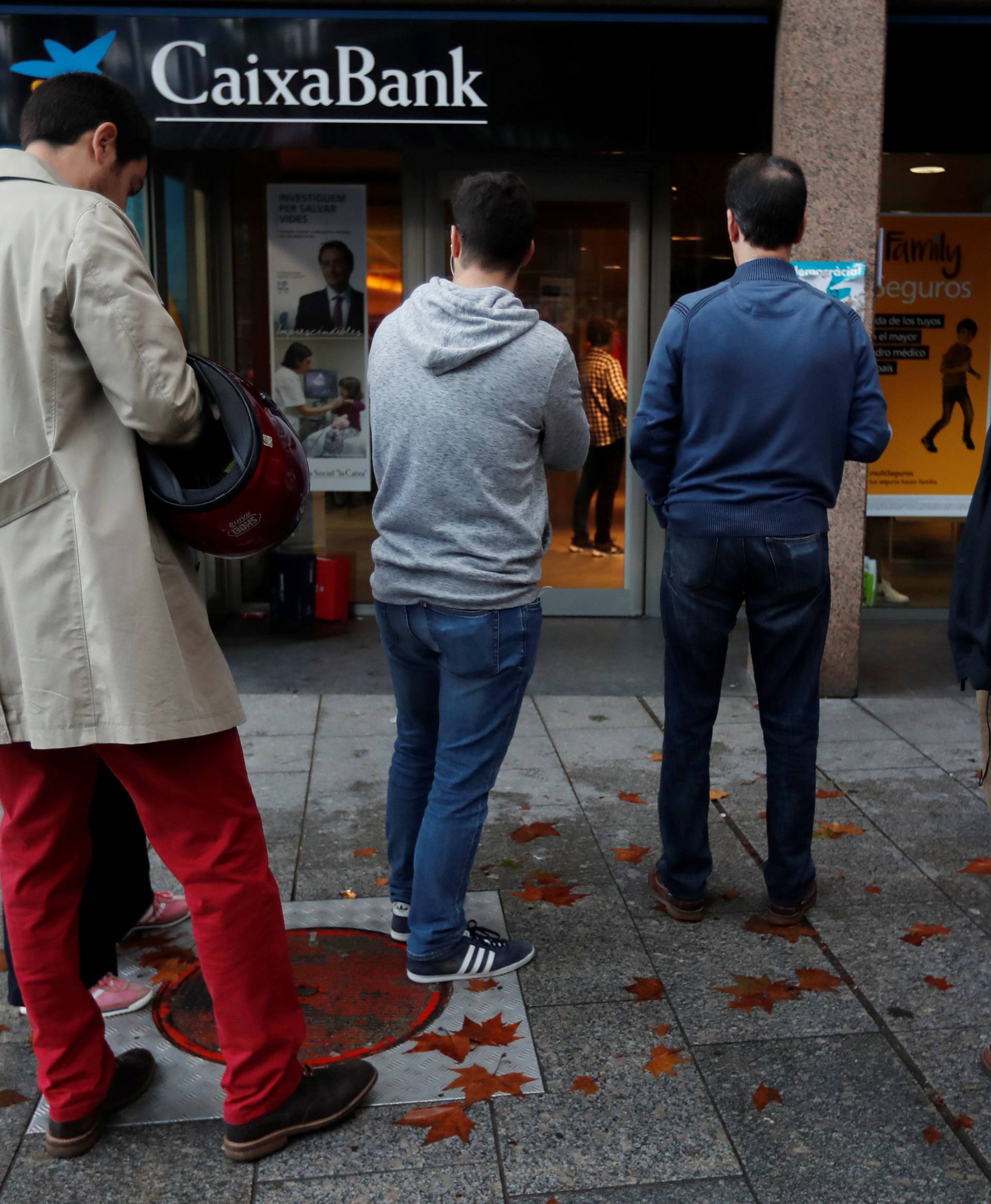 People line up at a cashpoint of La Caixa bank branch to withdraw money as part of an action to protest the transfer of the bank's headquarters out of Barcelona