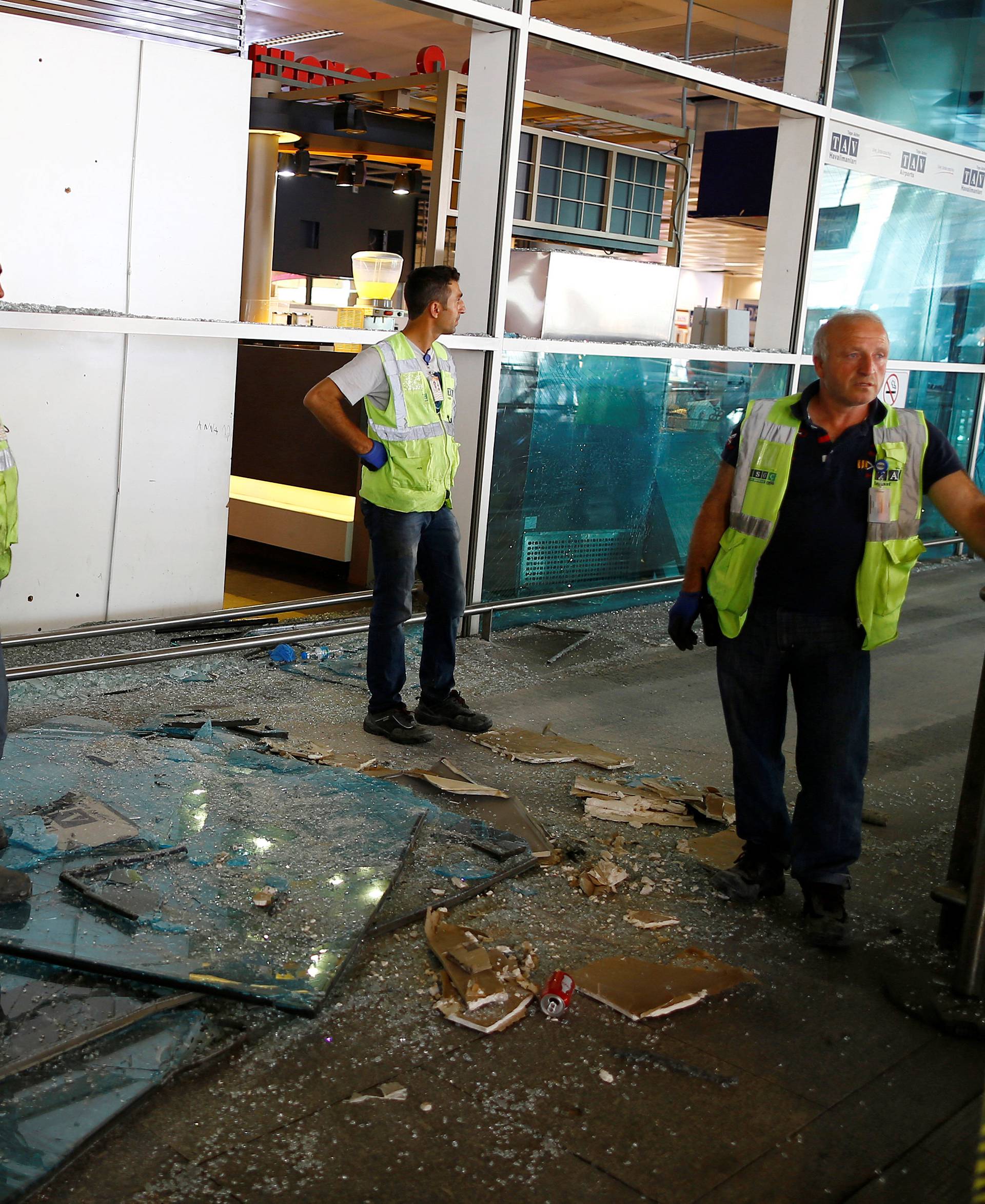 Workers stand near debris from yesterday's blasts as they take a break at Turkey's largest airport, Istanbul Ataturk