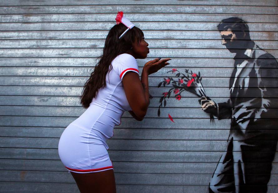 A dancer poses with a new installation of art by British graffiti artist Banksy painted on the front door of the Hustler Club in New York