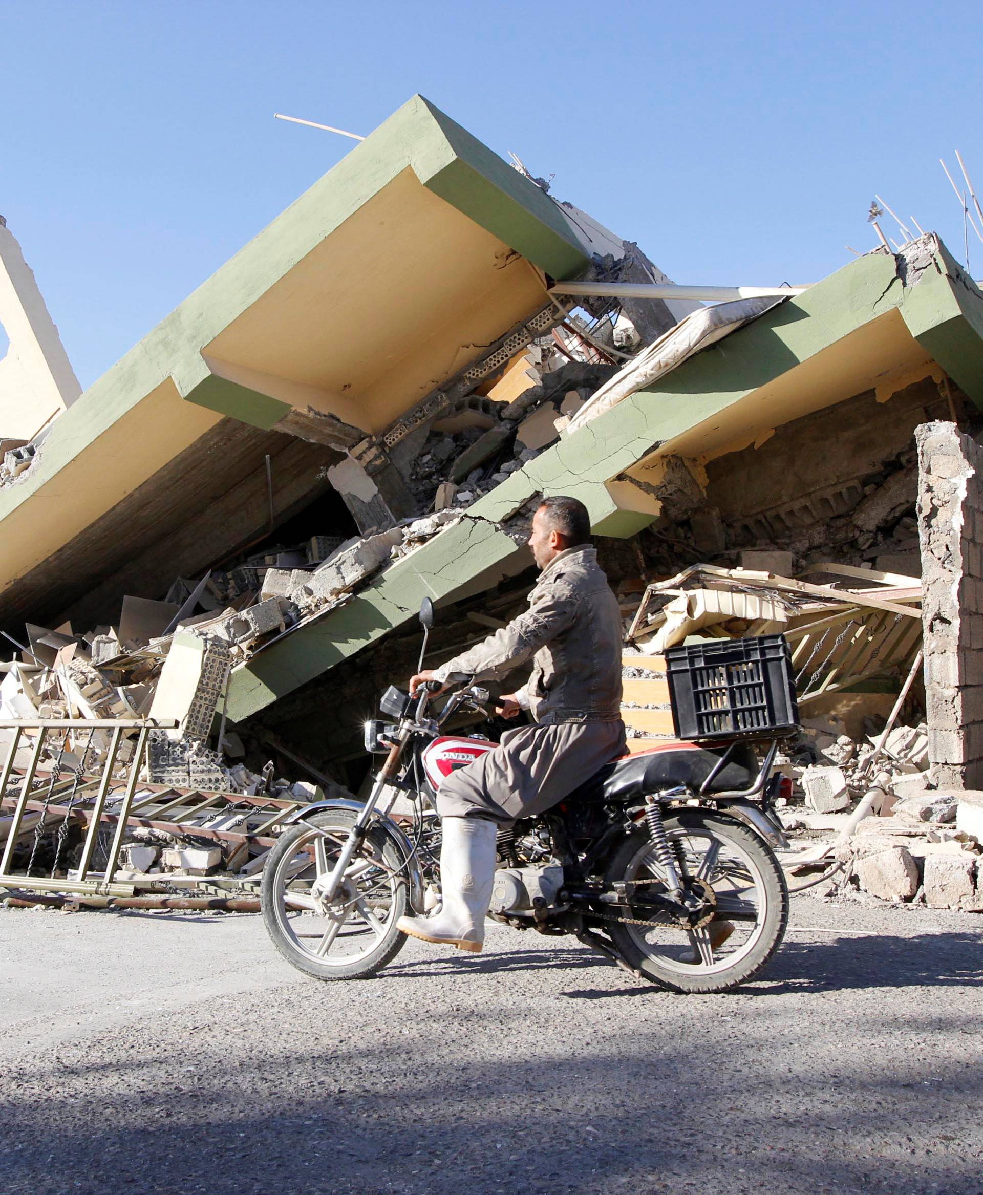 A man rides a motorcycle past a damaged building following an earthquake in the town of Darbandikhan