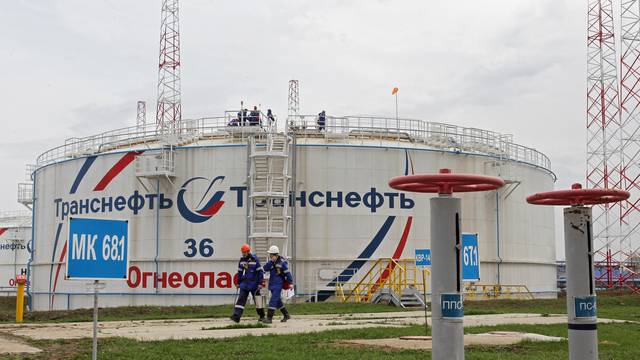 Workers walk past a storage tank at the Kaleikino oil pumping station near Almetyevsk