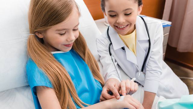 girl doctor putting medical plaster on hand of little patient