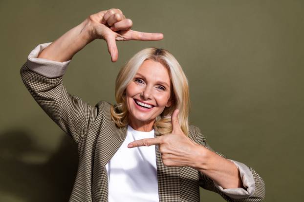 Portrait of smiling pretty woman experienced photo production art director showing frame snapshot symbol isolated on khaki color background