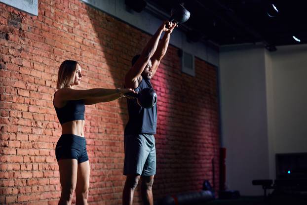 Sporty young couple with dumbbells on red brick wall background