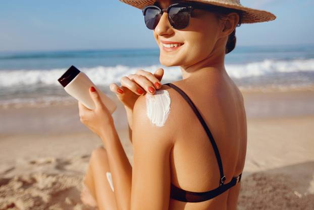 Beautiful Woman in Bikini Applying Sun Cream on Tanned  Shoulder. Sun Protection. Skin and Body Care. Girl Using Sunscreen to Skin. Portrait Of Female Holding Suntan Lotion and Moisturizing Sunblock.