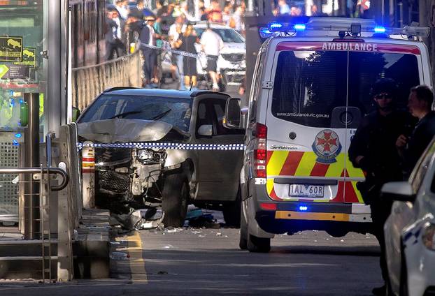 Australian police stand near a crashed vehicle after they arrested the driver of a vehicle that had ploughed into pedestrians at a crowded intersection near the Flinders Street train station in central Melbourne