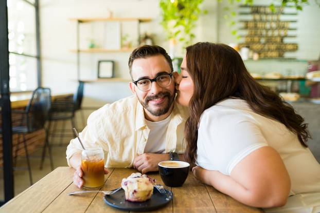 Zgodan srećan muškarac dobija poljubac u obraz od svoje plus size devojke u kafiću