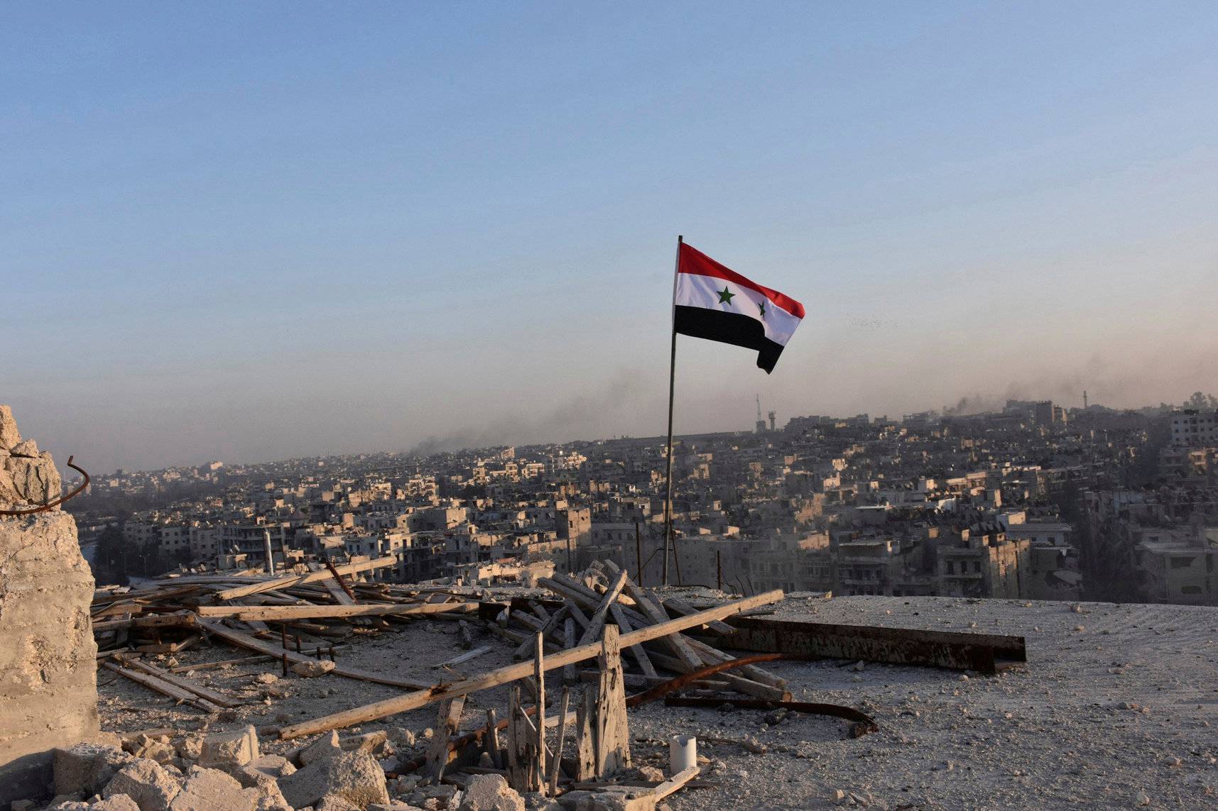 File photo shows Syrian national flag fluttering near a general view of eastern Aleppo after Syrian government soldiers took control of al-Sakhour neigbourhood in Aleppo