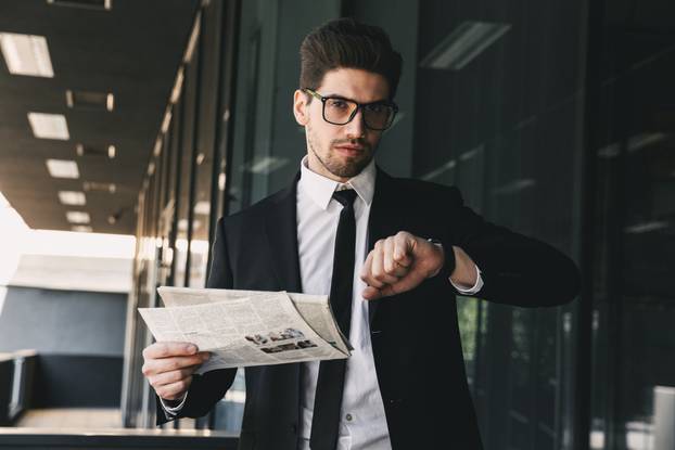 Business man holding newspaper looking at watch clock.