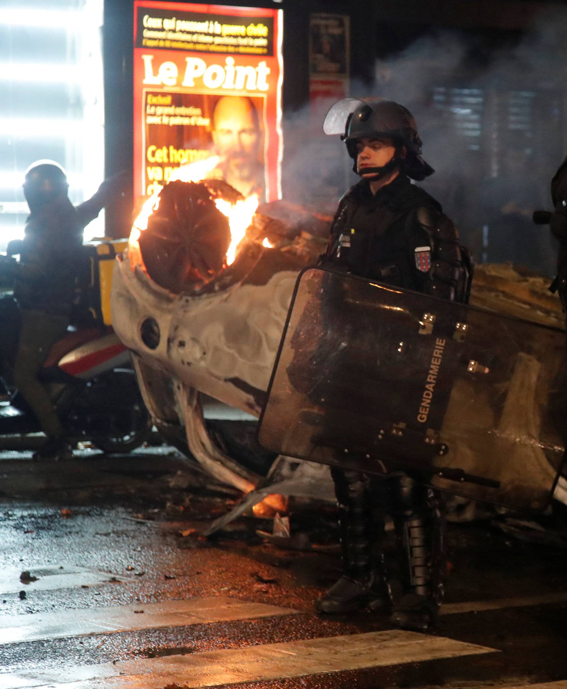 French riot police stand near an overturned burning car on avenue Kleber after clashes with protesters wearing yellow vests, a symbol of a French drivers' protest against higher diesel taxes, in Paris