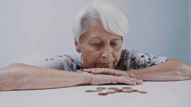 Sad face expression of old gray haired woman looking in few coins left on the table