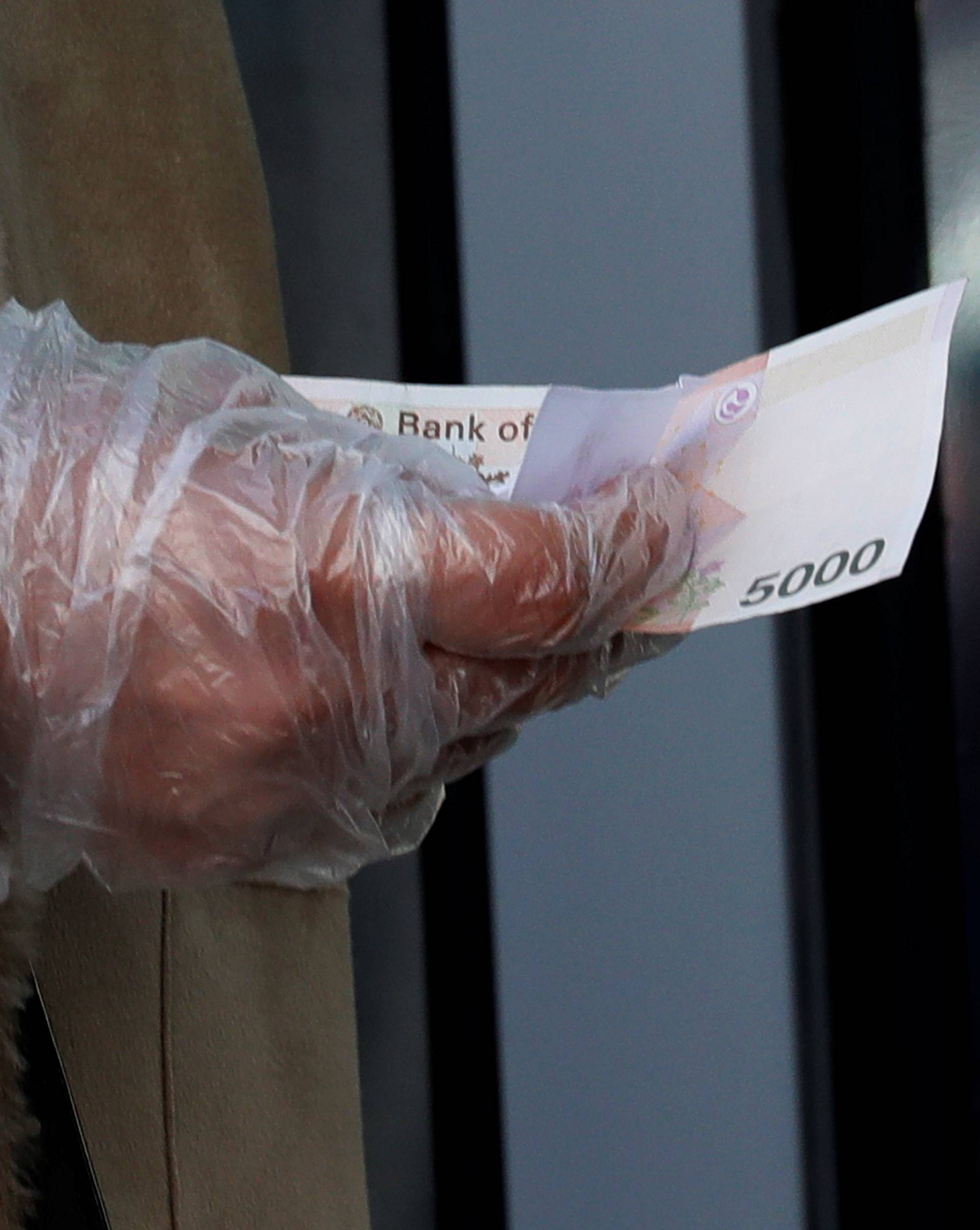 A woman wearing a plastic glove holds money as she stands in a queue to buy face masks amid the rise in confirmed cases of the novel coronavirus in Daegu