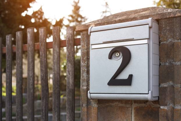 Metal mailbox with number 2 on stone fence near wooden gate outd