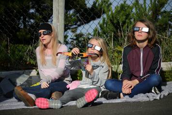 People use solar viewing glasses as the sun emerges through fog cover before the solar eclipse in Depoe Bay