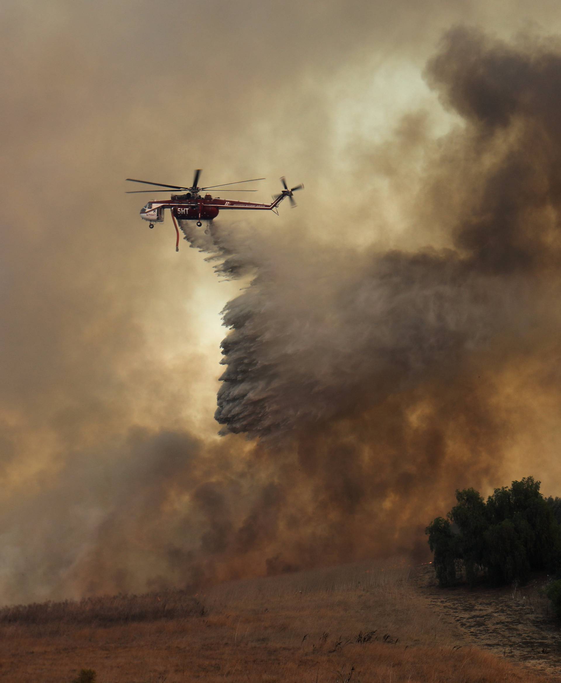 A firefighting helicopter drops water to help save a home during a wind driven wildfire in Orange, California