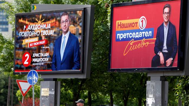 People walk past campaign billboards for the upcoming parliament and presidential elections in Skopje