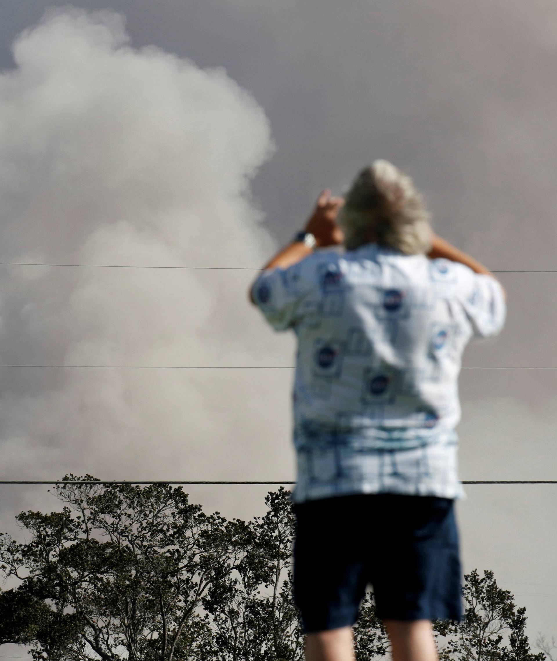 A man takes a photo as ash erupts from the Halemaumau Crater near the community of Volcano