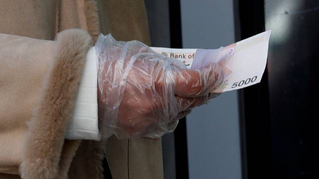 A woman wearing a plastic glove holds money as she stands in a queue to buy face masks amid the rise in confirmed cases of the novel coronavirus in Daegu