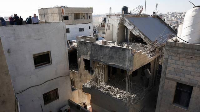 People look on near a house, damaged during an Israeli forces raid, in Qalandya