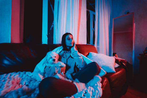 Beautiful young girl at home in a dark room playing with her dog and sits in front of a monitor or TV.