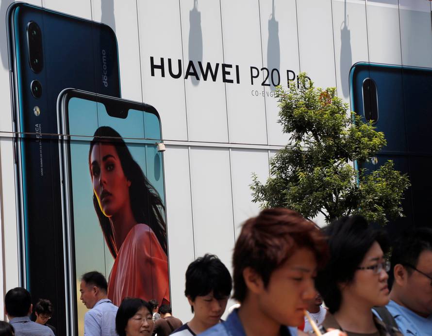 People walk past an advertisement for Huawei outside an electronic store in Tokyo