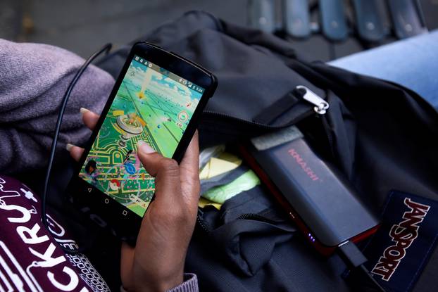 A woman uses a portable battery pack to charge her phone while playing the augmented reality mobile game "Pokemon Go" by Nintendo in New York City