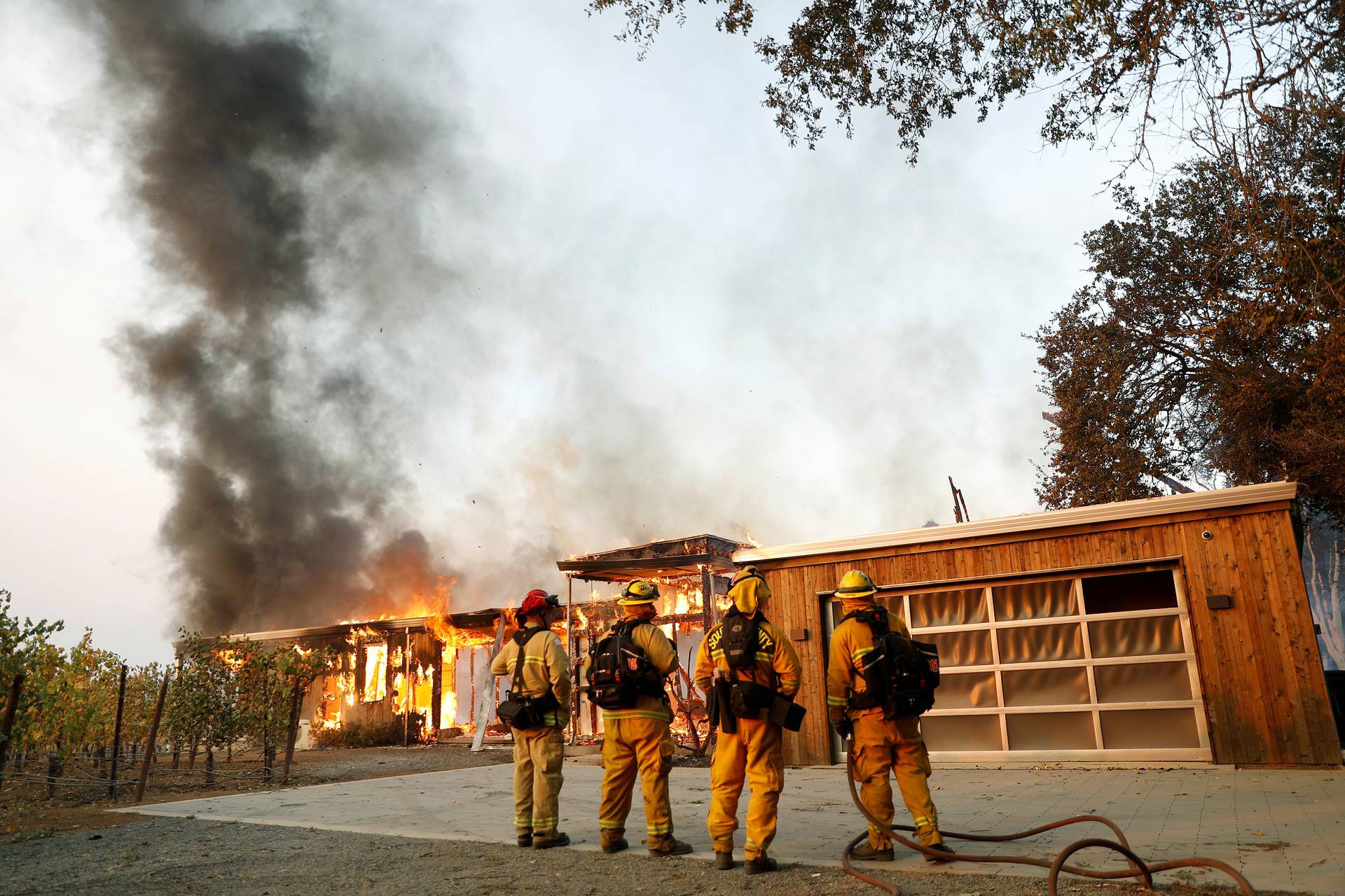 FILE PHOTO: A group of firefighters look on as a house burns during the wind-driven Kincade Fire in Healdsburg, California