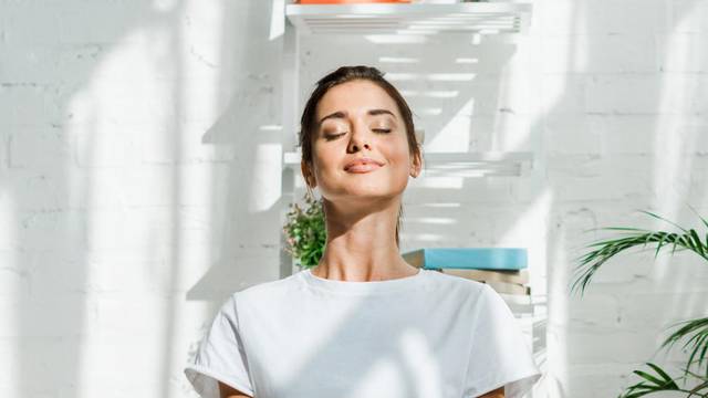 beautiful happy girl with closed eyes practicing yoga in lotus position in bedroom in the morning