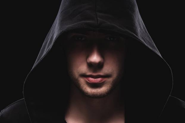 Close-up portrait of a courageous man in a deep dark hood on a black background. The concept of secrecy of secrets and people hiding from the government. Hackers and thieves. Low key