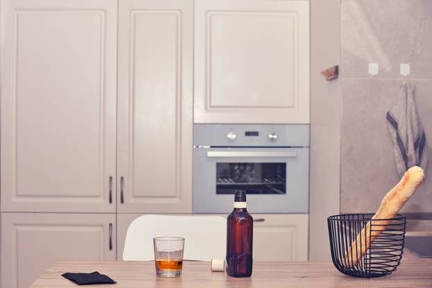 Empty chair, medical mask, glass with alcohol and bottle of whiskey on the kitchen table. Empty house with no people and a glass of whiskey, nobody