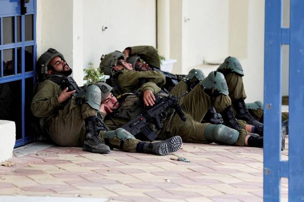 Israeli soldiers rest near a building the day after a mass infiltration by Hamas gunmen from the Gaza Strip, in Sderot
