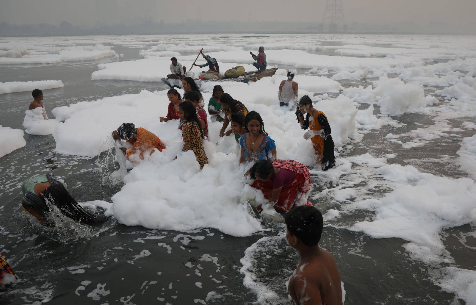 People bathe amidst the foam covering the polluted Yamuna river on a smoggy morning in New Delhi