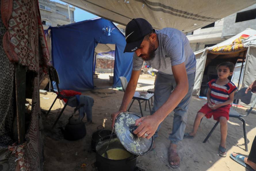 Displaced Palestinian man Nizar Bakron cooks at his tent in Gaza City