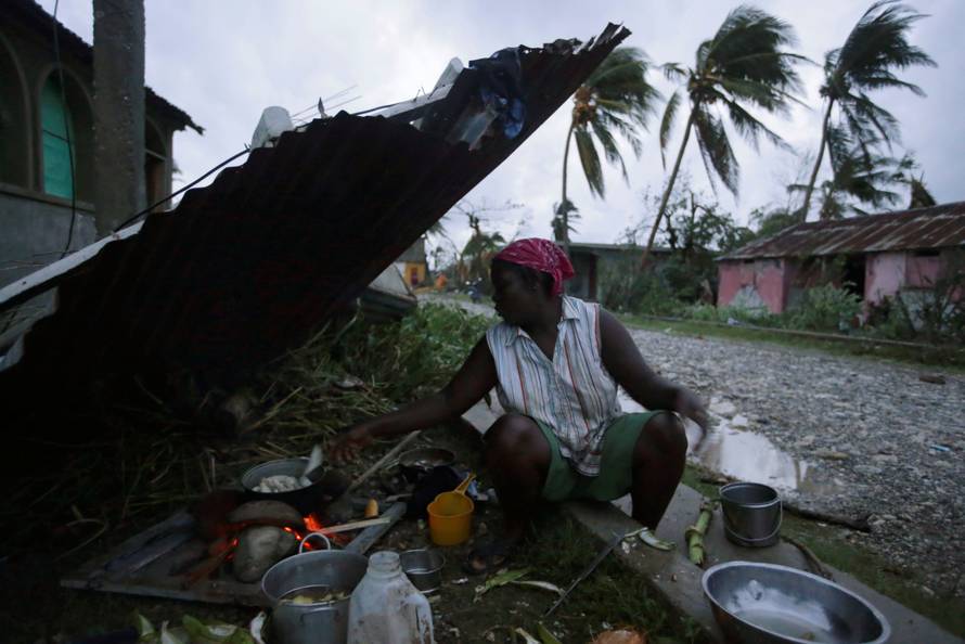 A woman cooks next to a house damaged by Hurricane Matthew in Les Cayes