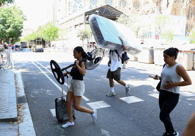 A woman carrying a fan and a trolley bag walks next to Sagrada Familia Basilica during a heatwave in Barcelona