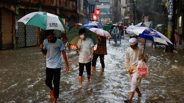 People wade through a flooded street, amid continuous rain before the Cyclone Sitrang hits in Dhaka