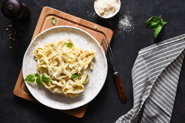 Tagliatelle pasta with cheese sauce and basil in a plate on the kitchen table.