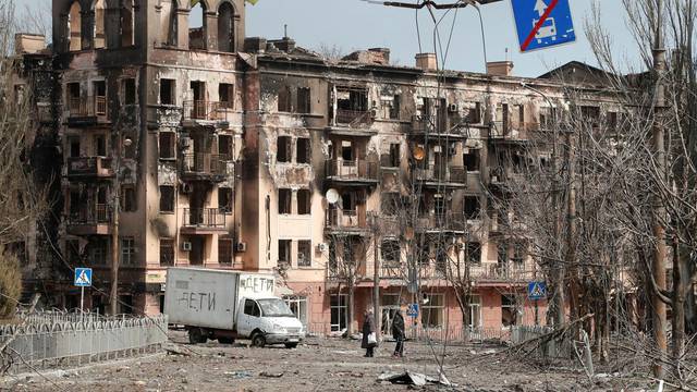 Local residents walk along a street next to a damaged building in Mariupol