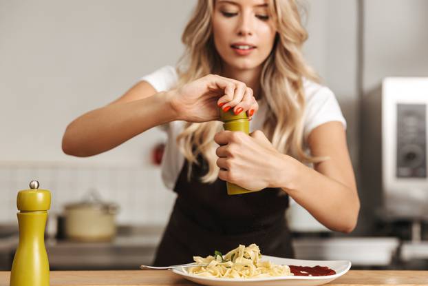 Pretty young woman chef putting salt