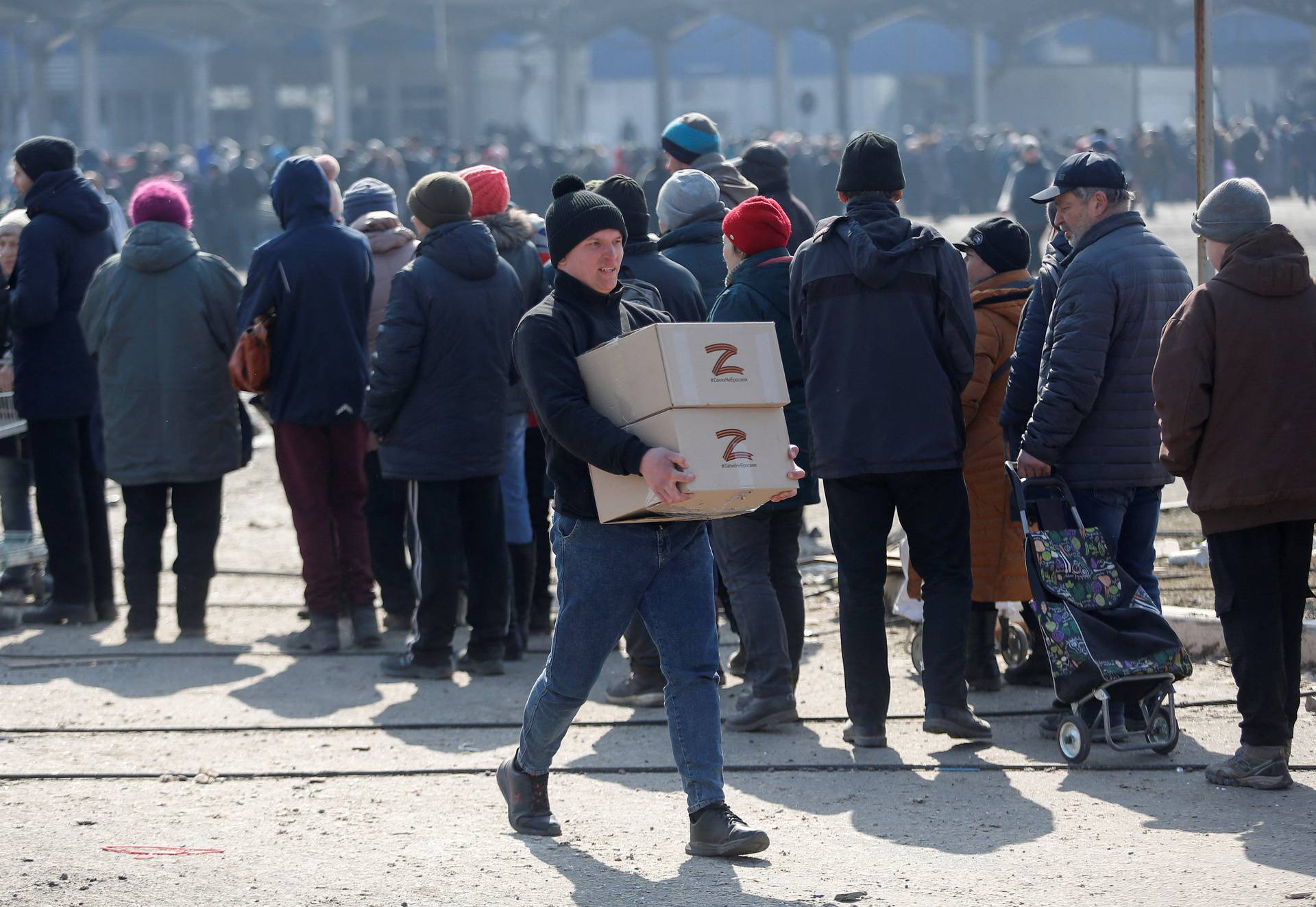 People stand in a line during the distribution of humanitarian aid in the besieged city of Mariupol